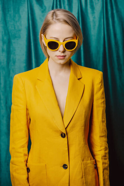 Stylish ukrainian woman in yellow sunglasses and jacket on green curtains background