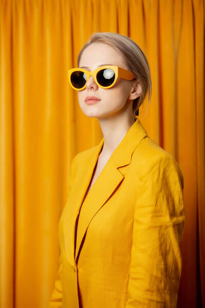 Stylish ukrainian woman in yellow sunglasses and jacket on curtains background
