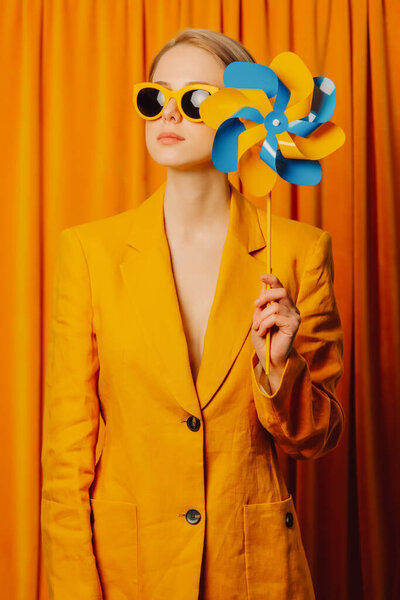 Stylish ukrainian woman in yellow sunglasses and jacket with pinwheel on curtains background