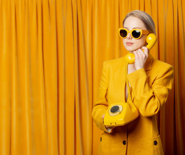 Stylish ukrainian woman in yellow sunglasses and jacket with dial phone on curtains background