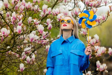 Beautiful blond woman in sunglasses and blue shirt next to Magnolia tree in spring time