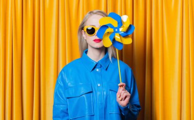 Stylish woman in blue shirt and yellow sunglasses with pinwheel in ukrainian flag colors 