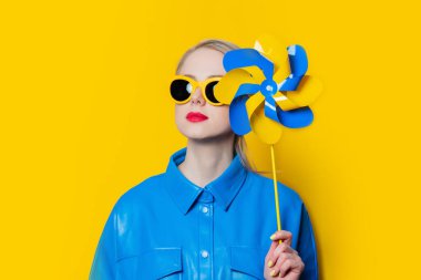 Stylish ukrainian woman with pinwheel in urkaine flag colors on yellow background