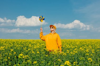 Ulusal bayrak renginde fırıldak taşıyan şık Ukraynalı kadın bahar zamanı kolza tohumu tarlasında