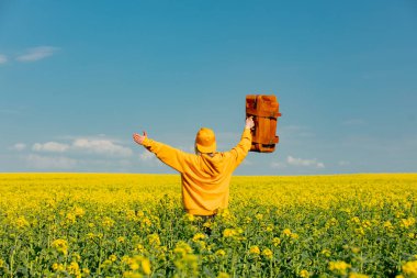 Sarı kapüşonlu Ukraynalı kadın kolza tarlasında çanta taşıyor.