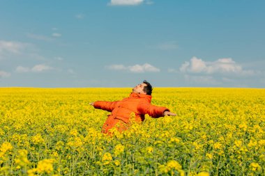 Kolza tarlasında turuncu ceketli şık bir adam.