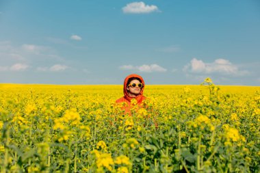 Kolza tarlasında turuncu ceketli şık bir adam.