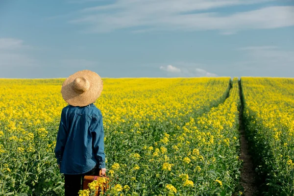 Woman in hat with suitcase in rapeseed field