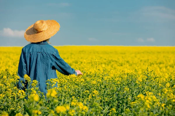 Kolza tarlasında şapkalı ve mavi gömlekli bir kadın.