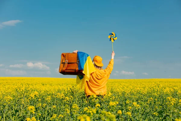女性で黄色パーカーでピンホイールとスーツケースでRapeseedフィールド — ストック写真