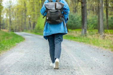 Woman with backpack walking on road in forest in spring time