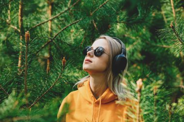 Kapüşonlu şık kız, çam ağacı ormanlarında kulaklıkla müzik dinliyor.