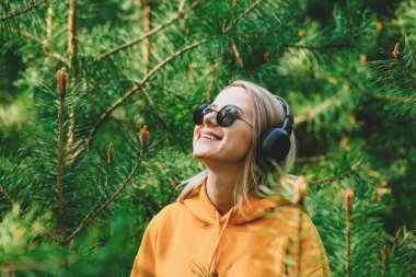 Kapüşonlu şık kız, çam ağacı ormanlarında kulaklıkla müzik dinliyor.
