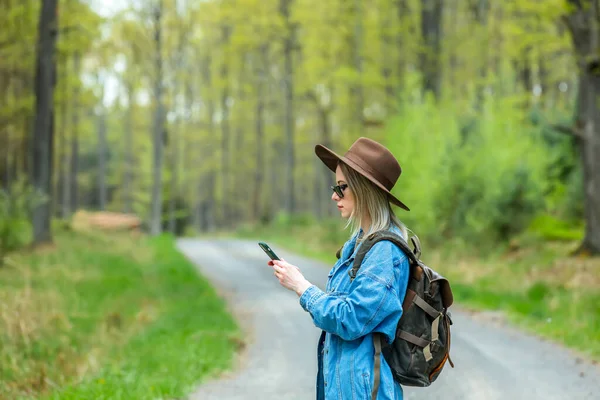 Şapkalı ve sırt çantalı şık bir kadın açık havada cep telefonuyla fotoğraf çeker.
