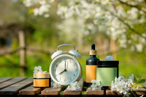 Klasik çalar saat ve kozmetik şişe ve kavanoz ahşap masa baharı bahçesinde. 
