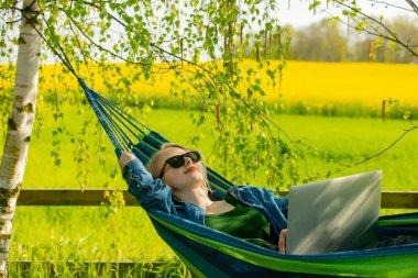Hamaktaki kadın kırsal kesimdeki hamakta dizüstü bilgisayarla çalışıyor.