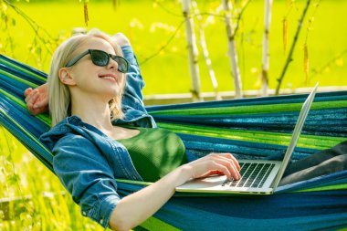 Hamaktaki kadın kırsal kesimdeki hamakta dizüstü bilgisayarla çalışıyor.