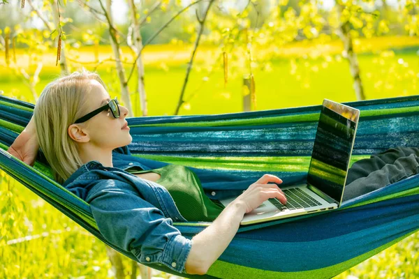 Hamaktaki kadın kırsal kesimdeki hamakta dizüstü bilgisayarla çalışıyor.