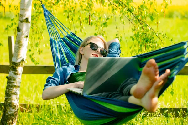 Hamaktaki kadın kırsal kesimdeki hamakta dizüstü bilgisayarla çalışıyor.