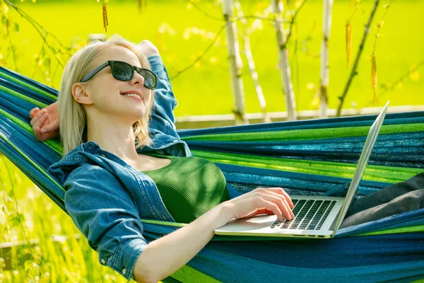 Hamaktaki kadın kırsal kesimdeki hamakta dizüstü bilgisayarla çalışıyor.