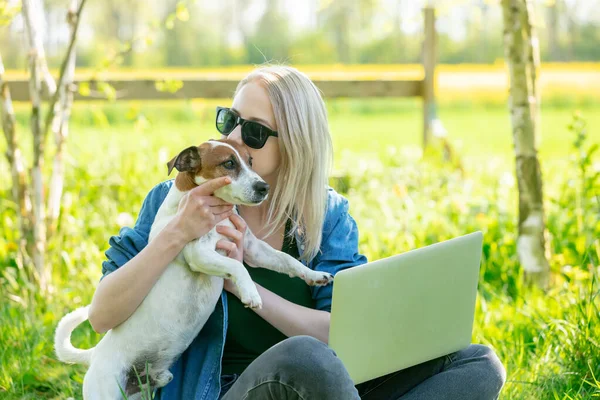 Bahçede bir köpekle dizüstü bilgisayarda çalışan bir kadın.
