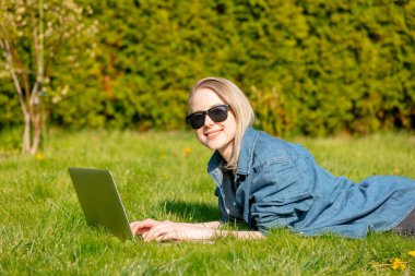 Bahçedeki çimlerin üzerinde bilgisayarı olan bir kadın