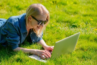 Bahçedeki çimlerin üzerinde bilgisayarı olan bir kadın