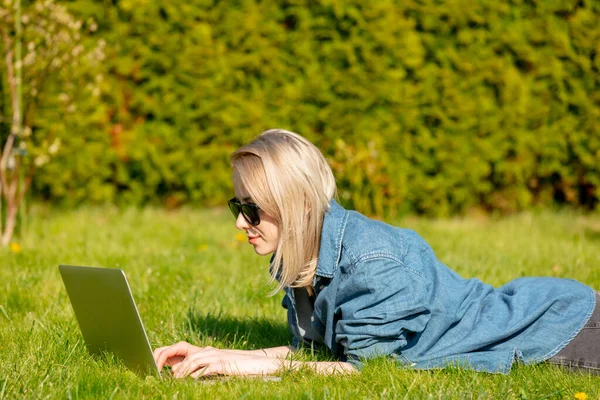 一个带着电脑的女人躺在花园里的草地上 — 图库照片