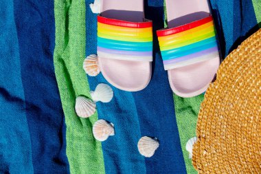 Renkli parmak arası terlikler ve havluda şapkası olan kabuklar.