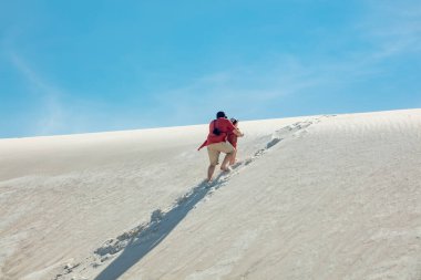 father helps his son up a sand dune in desert