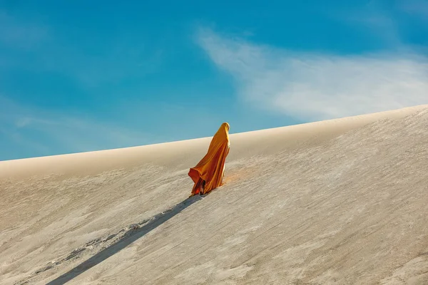 穿着阿拉伯黄色衣服的女人爬上沙漠中的沙丘 — 图库照片