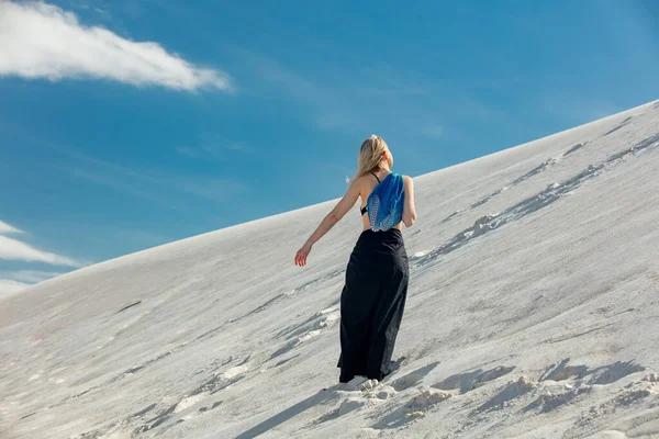 Woman with blue net bag walking on white sand dune in desert in summer