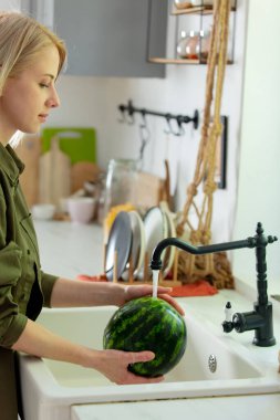 Kadın mutfakta lavaboda karpuz yıkıyor. 
