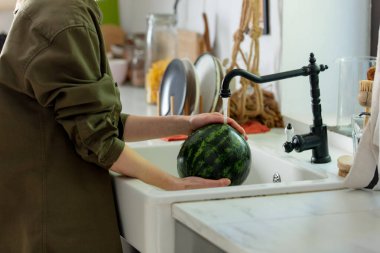 Kadın mutfakta lavaboda karpuz yıkıyor. 