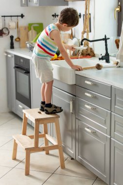 Küçük çocuk mutfakta tabak yıkıyor.