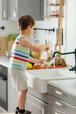 Küçük çocuk mutfakta tabak yıkıyor.