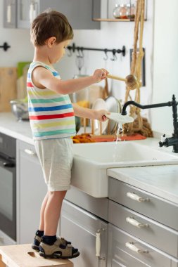 Küçük çocuk mutfakta tabak yıkıyor.