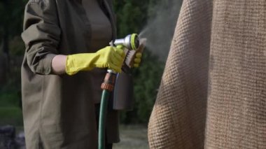 Kadın dışarıda çevre dostu bir halı yıkıyor ve ıslatıyor.