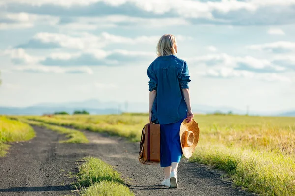 夏天穿着蓝色衣服提着手提箱走在乡间路上的女孩 — 图库照片