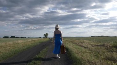 Polonya 'da kırsal yolda bavullu bir kadın yürüyor.