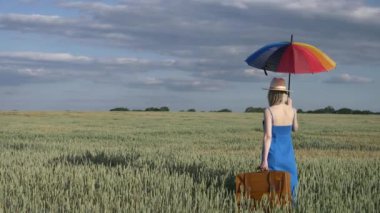 Buğday tarlasında şemsiyeli ve valizli kadın