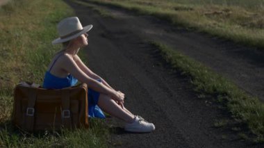 Bavullu kadın kırsal yolda oturuyor.