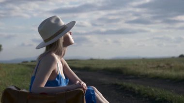 Bavullu kadın kırsal yolda oturuyor.