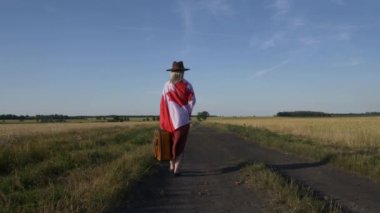 Kanada bayrağında bavullu bir kız gün batımında köy yolunda