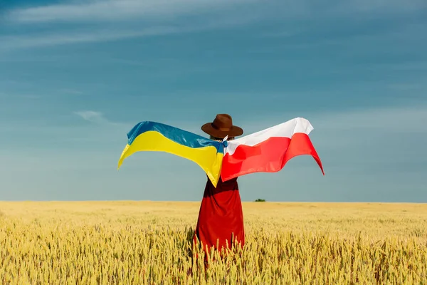 Girl with Ukraine and Poland flags in wheat field and blue sky on background