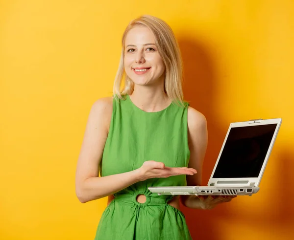 黄色の背景にラップトップコンピュータと緑のドレスのスタイリッシュな女の子 — ストック写真