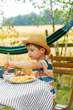 Küçük çocuk bahçede oturmuş salata ve patates kızartması yiyor.