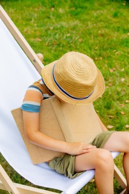 Funny little boy with a book sits in chair in outdoor
