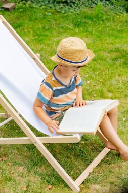 Kitaplı küçük komik çocuk, dışarıda sandalyede oturuyor.