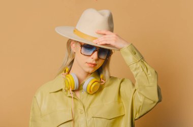 Stylish 80s woman in eyeglasses, headphones and hat on brown background